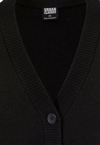 Svart strikket cardigan med ribbestrikket krage, med enkelt knappelukking og en merkelapp merket "Urban Classics" i kragen.