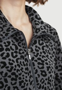 Grå zip-tröja i mjuk fleece med svart leopardmönster. Har hög krage och silverdetalj på dragkedjan. Slät textur.