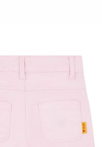 Pantalons en denim rose clair avec poches arrière, passants de ceinture et un petit logo ours brodé. Une étiquette jaune accentue la poche gauche.