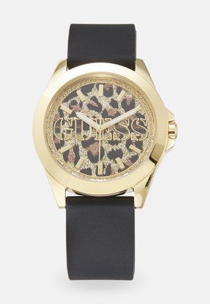 Zlaté hodinky s čiernym silikónovým remienkom. Okrúhly ciferník má leopardský vzor a zlaté logo "GUESS", so zlatými číslicami a ručičkami.