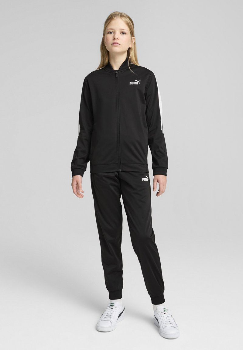Survêtement noir avec une veste zippée et un pantalon assorti, présentant des accents blancs sur les manches et un petit logo sur la poitrine. Tissu lisse.