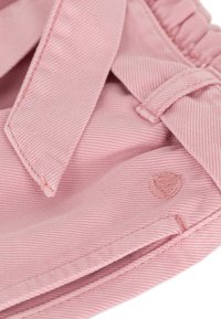 Roze stof met een gestructureerde afwerking, voorzien van een strikdetail en een klein ingebosseld logo. Zichtbare stiksels in een bijpassende tint.