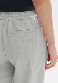 Pantalons gris clair avec une texture subtile, dotés d'une taille élastique et d'une poche arrière simple. Tissu lisse sans motifs visibles.