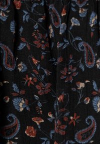 Svart tyg med blommig och paisleymönster i blått, rött och krämfärgat, med en mjuk textur och subtila veck.