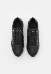 Chaussures de sport noires avec une tige en cuir lisse, un bout rond et une semelle blanche contrastante. Elles sont dotées d'une fermeture à lacets et du logo de la marque sur la languette.