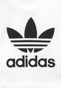 White cotton t-shirt featuring a large black Adidas trefoil logo and “adidas” text below in bold sans-serif font.