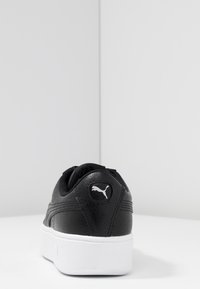 Sneaker in pelle nera con finitura testurizzata, suola in gomma bianca e un logo bianco ben visibile sul tallone. Caratteristiche: punta arrotondata e colletto imbottito.