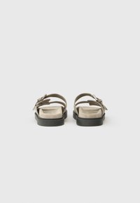 Sandale gri cu un barete lată, textură moale similară cu suede, și o talpă din cauciuc negru. Prezintă o fundă decorativă pe lateral.