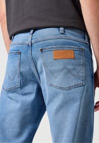Ljust blå denimjeans med rak skärning, med två bakfickor och en ljus läderlapp med "Wrangler" präglat på.