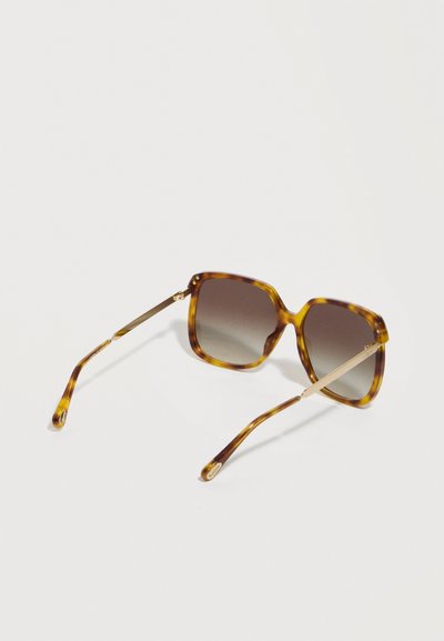 Γυαλιά ηλίου σε σχήμα τετράγωνου χελωνόστρακα με καφέ φακούς διαβαθμισμένου χρώματος και μεταλλικά χρυσά μπράτσα, εμφανίζονται σε λευκό φόντο.