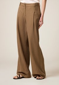 Bruna strimmiga vida byxor med framveck, med midja med bältesöglor och metallknappsstängning.