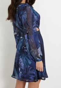 Robe à imprimé floral dans des nuances de marine et de bleu, dotée de longues manches transparentes, de détails découpés et d'une texture fluide et douce.