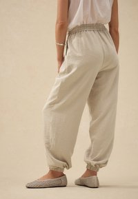 Heledast beežid, tekstuuriga jogger-püksid, millel on elastne vöökoht ja mansetid, kombineeritud hallide, kootud madalate kingadega. Lihtne, lõdvestunud lõikega disain.