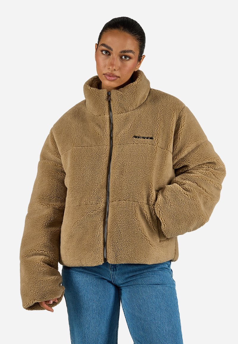 Giacca in pile marrone con zip e colletto alto, vestibilità oversize e due tasche per le mani. Presenta un tessuto testurizzato e un branding minimale sul petto.
