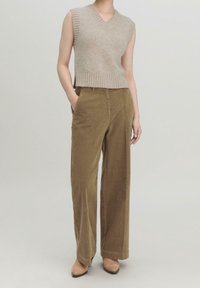 Beige svetr bez rukávů s žebrovaným lemem, doplněný širokými kalhotami z olivového kordu. Oba kousky mají strukturovaný povrch.