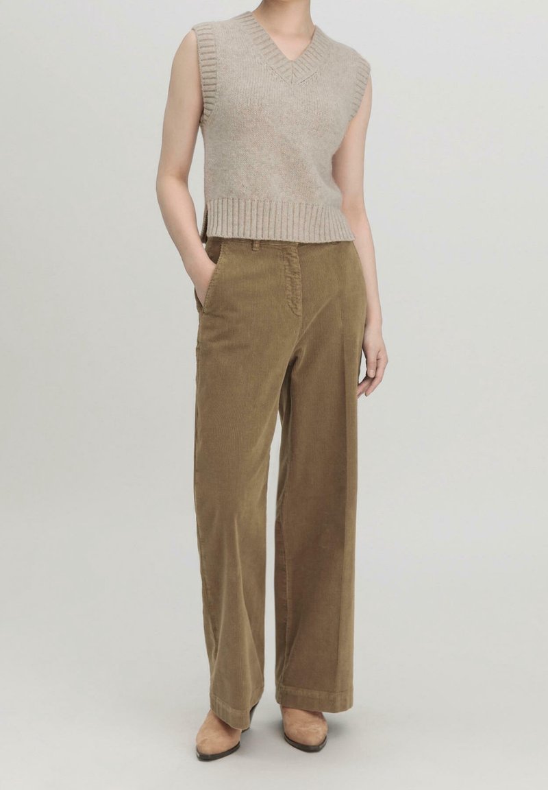 Beige svetr bez rukávů s žebrovaným lemem, doplněný širokými kalhotami z olivového kordu. Oba kousky mají strukturovaný povrch.