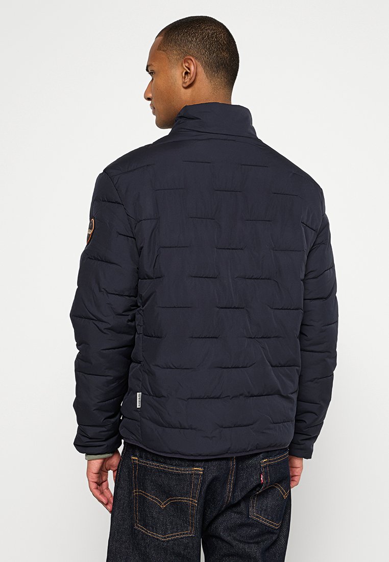 Marineblaue Steppjacke mit hohem Kragen, Karomuster und einem Logo-Patch am Ärmel. Hergestellt aus glattem, leichtem Stoff.