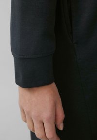 Schwarzer Sweatshirtstoff mit einem Manschetten-Detail. Die Manschette hat einen umschlagenen Rand, der eine glatte Textur zeigt, mit einer leicht lockeren Passform am Handgelenk.