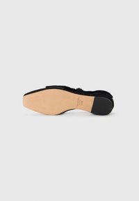 Black suede flat shoe with a smooth, rounded toe and a flexible sole. Features a subtle bow detail on the front and a light-colored insole.