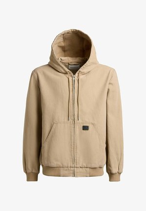 Beżowa bluza na zamek z przednimi kieszeniami typu kangur, kapturem ze sznurkiem, ściągaczami na mankietach oraz małą czarną naszywką na kieszeni.