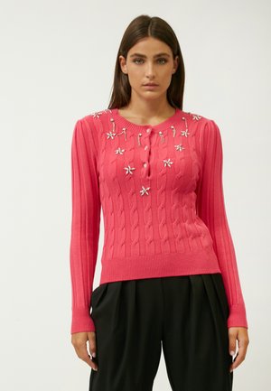 Gestrickter, gerippter Pullover mit langen Ärmeln in leuchtendem Pink, mit einem geknöpften Ausschnitt und floralem Schmuck auf der Vorderseite.