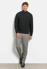 Dunkelgrauer Reißverschluss-Pullover mit hohem Kragen, kombiniert mit hellgrauer Hose und dunklen Sneakers, was ein ausgewogenes, lässiges Outfit ergibt.