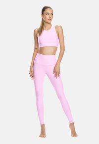 Světle růžový sportovní crop top a legíny s vysokým pasem vyrobené z elastického materiálu, s bezešvým designem a hladkou texturou.