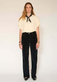 Haut jaune clair à manches courtes, pantalon en velours côtelé noir taille haute, bracelets en argent et chaussures noires à bout pointu avec des accents métalliques.