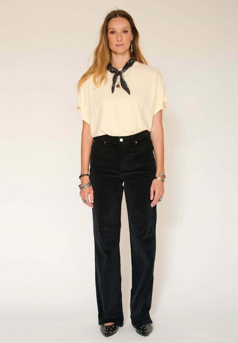 Haut jaune clair à manches courtes, pantalon en velours côtelé noir taille haute, bracelets en argent et chaussures noires à bout pointu avec des accents métalliques.