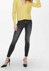 Žlutý žebrovaný cardigan s hlubokým výstřihem do V, zapínání na knoflíky; kombinovaný s tmavými skinny džíny a černými lodičkami na vysokém podpatku.