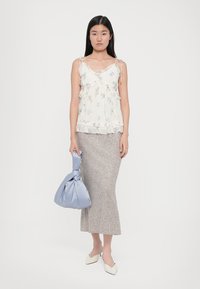 Mit Blumenmuster bedrucktes, cremefarbenes Tanktop mit Rüschensaum, kombiniert mit einem grauen strukturierten Rock in Knielänge. Das Model hält eine hellblaue Satin-Handtasche.