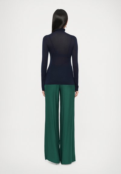 Tumesinine pikaaegne kaelusega top, millel on liibuv lõige, kombineeritud laia säärega metsaroheliste pükstega, sile tekstuur ja nähtavad mustrid puuduvad.