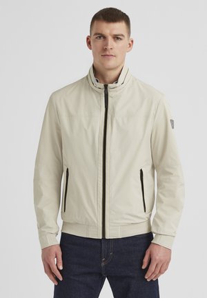 Light beige jacket with a high collar, front zip closure, and two side zip pockets. Features ribbed cuffs and hem, smooth fabric texture.