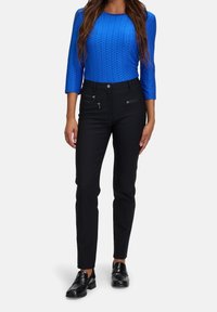 Niebieska, teksturowana bluzka z długim rękawem i okrągłym dekoltem, w połączeniu z czarnymi spodniami slim-fit z podwójnymi kieszeniami na zamek, noszone z czarnymi loafersami.