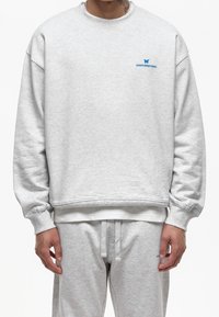 Grijze trui met een ronde hals, geribbelde manchetten en een subtiel blauw logo. De stof lijkt zacht met een licht gestructureerde afwerking.