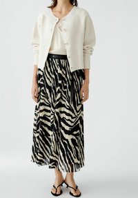 Gilet blanc tricoté avec texture côtelée, fermeture à boutons ; jupe maxi plissée noire et crème à rayures zèbre avec taille noire et liens.