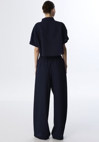 Marine tweed outfit bestaande uit een cropped top met korte mouwen en hoge wijde broek, gemaakt van een gestructureerde stof.