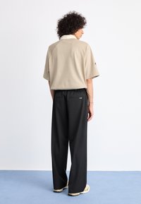 Beige short-sleeve collared shirt with raglan sleeves, paired with loose black trousers featuring back pockets, worn with light sneakers.