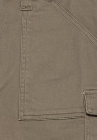 Brązowa tkanina płócienna z ukośnym przeszyciem. Posiada kieszeń naszywaną oraz widoczne detale szwów, ukazujące trwałą i wytrzymałą fakturę.