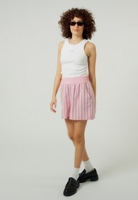 Balta liemenėlė su logotipu, šviesiai rožinės dryžuotos šortai su elastinga juosmens juosta ir kišenėmis, derinami su juodais masyviais batais ir baltais kojinėmis.