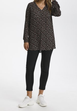 Tunique noire à fleurs avec des manches longues et un col en V, associée à des leggings noirs et des baskets blanches. La tunique présente une coupe ample et des détails subtils.