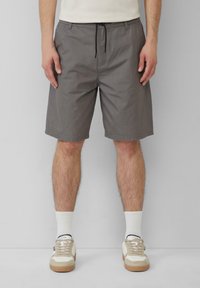 Grau gemusterte Shorts mit einem Kordelzugbund, seitlichen Taschen und einem entspannten Schnitt, kombiniert mit weißen Socken und lässigen Sneakers.