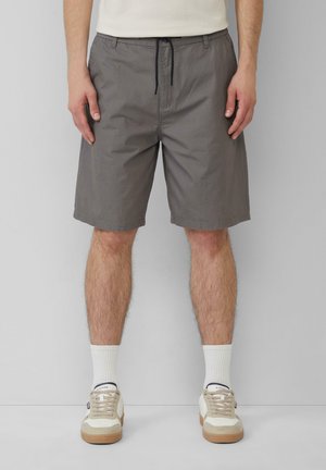 Shorts gris à motifs avec taille à cordon de serrage, présentant des poches latérales et une coupe décontractée, associés à des chaussettes blanches et des baskets casual.