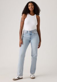 Jeans di denim azzurro chiaro con un fit dritto e vita alta, abbinati a un top a spalla bianco a coste. Il modello si trova su uno sfondo neutro.