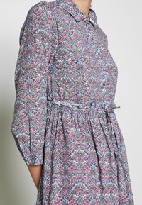 Blumenmusterkleid mit einem Knopfkragen, langen Ärmeln, elastischer Taille, in den Farbtönen Rosa, Blau und Weiß, aus leichtem Stoff.