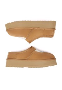 Tan slip-on shoes with a soft textured upper, white interior lining, and a thick beige rubber sole featuring a wavy tread pattern.