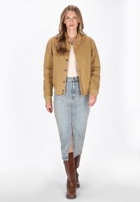 Barna vászon dzseki patentgombokkal, világos bézs felső és világoskék farmer szoknya elöl hasítékkal. Barna térd fölé érő csizmák csattokkal.