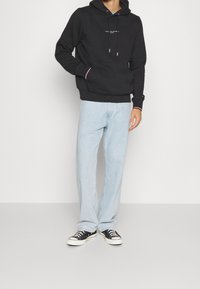 Czarna bluza z kapturem i sznurkiem, z przednią kieszenią i logo; zestawiona z jasnoniebieskimi spodniami typu straight-leg i czarnymi sneakersami.