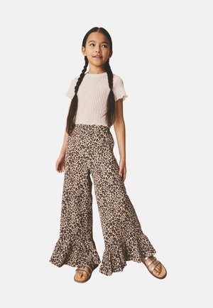 Young girl with long braids wearing light pink short-sleeve top, wide leopard-print pants with ruffled hems, and sandals.