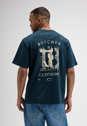 Man wearing dark blue graphic t-shirt with text and symbols on the back, paired with blue denim jeans, facing away from the camera.